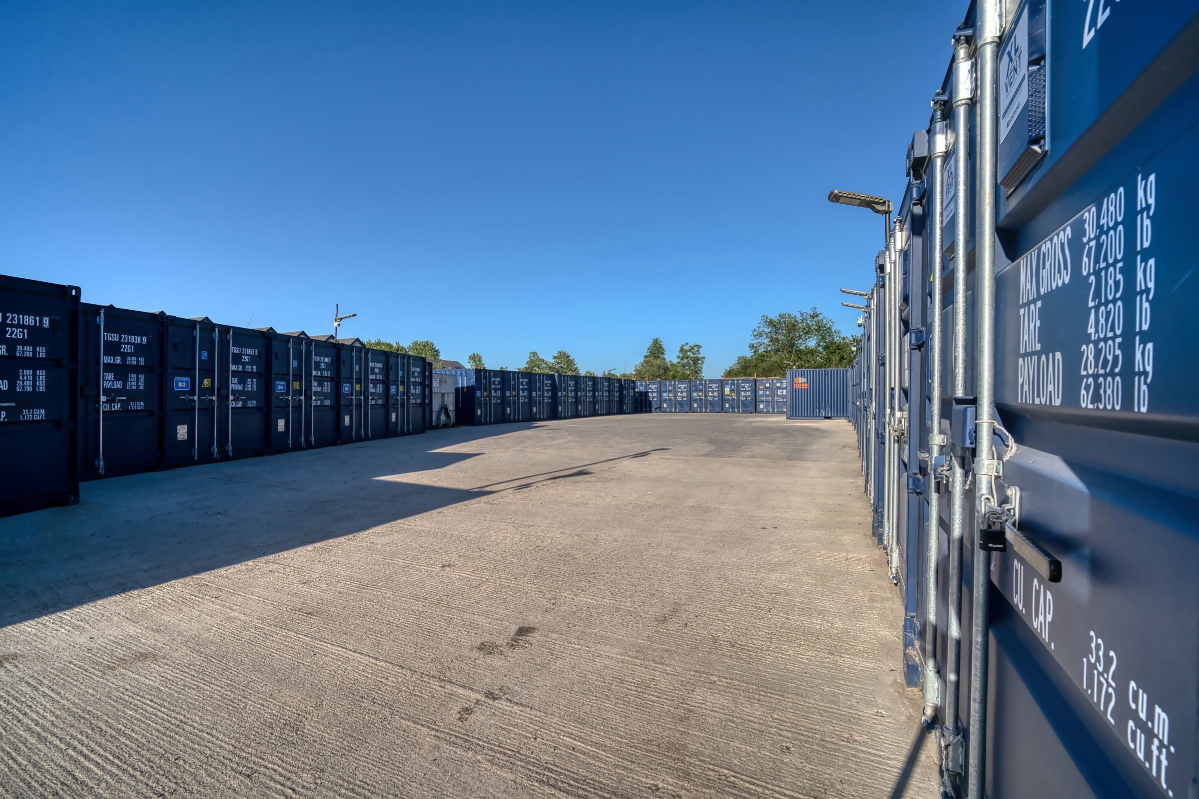 Long evening shadows stretching across the drive-up lane between angled rows of blue storage containers