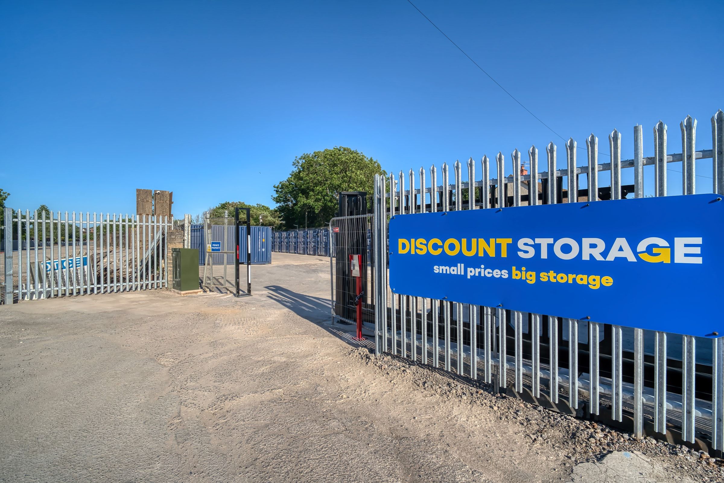 Open palisade security gate at the site entrance beside the blue Discount Storage banner