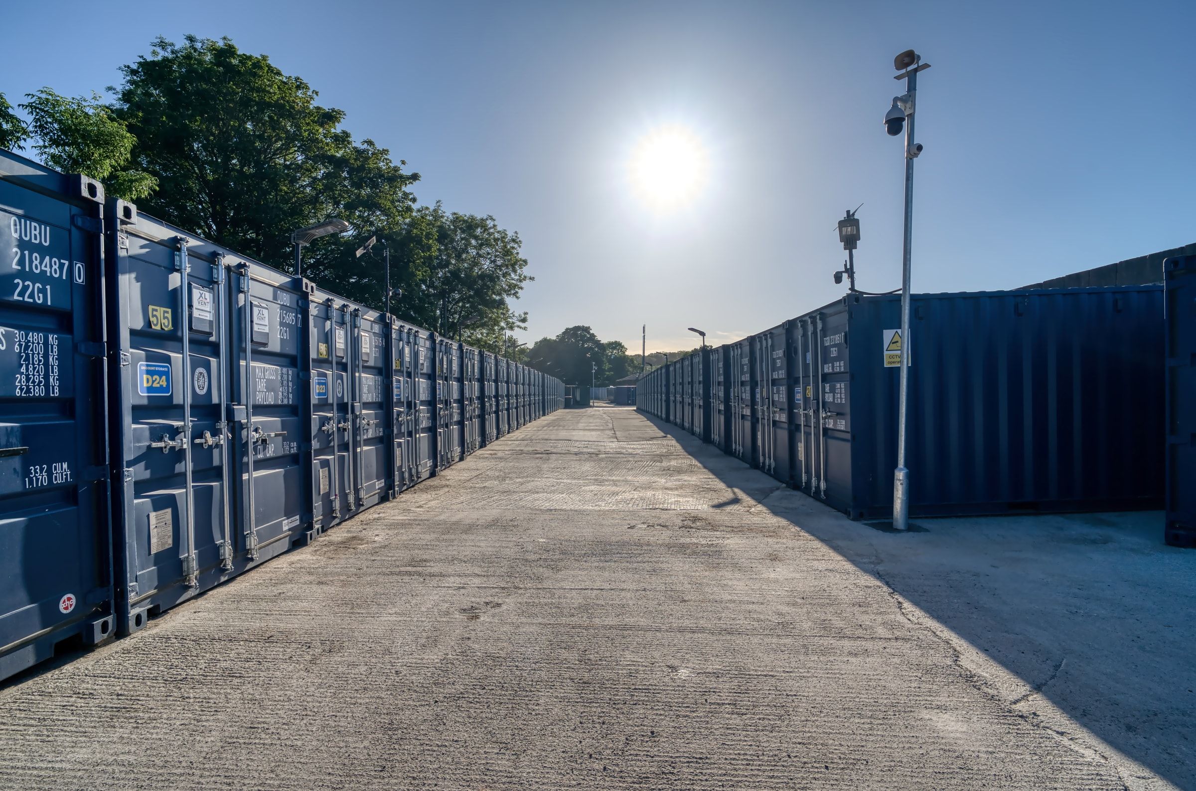 Storage container rows lit by low evening sun with a CCTV pole over the drive-up lane